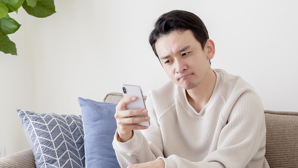 Asian,Man,Looking,At,Smartphone,In,Living,Room