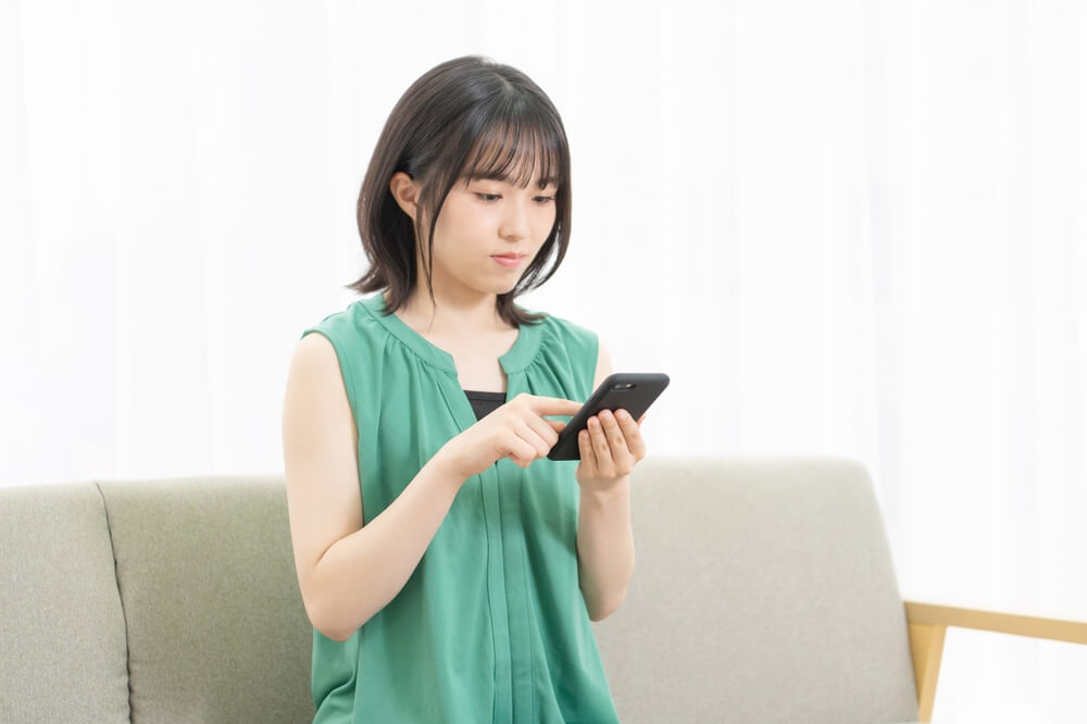 Young,Woman,Sitting,On,A,Sofa,And,Using,A,Smartphone