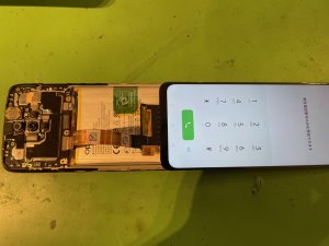 修理の途中で新しいディスプレイパネルを本体に仮付けし、液晶の映りやタッチ感度が正常かを入念にテストしている様子
